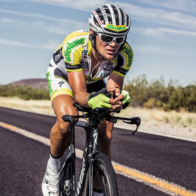 Un ciclista in una maglia gialla e nera e guanti guida su una strada, indossando un casco da ciclismo e occhiali da sole.