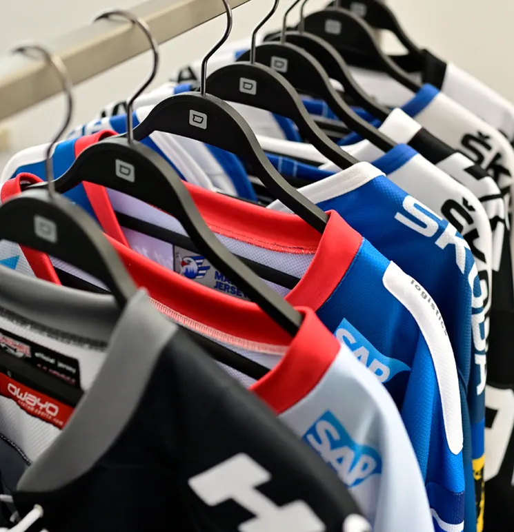 Una fila di maglie sportive colorate personalizzate di owayo appese a grucce nere su un portabiti.