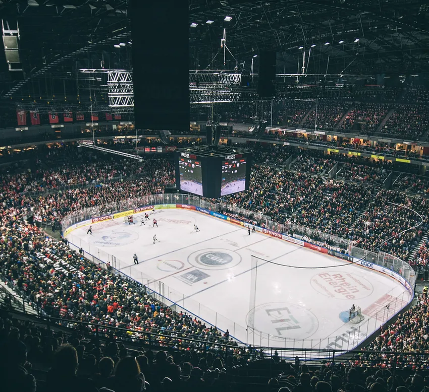 Una vista ampia di un'arena di hockey su ghiaccio affollata, con giocatori sul ghiaccio e un grande tabellone.