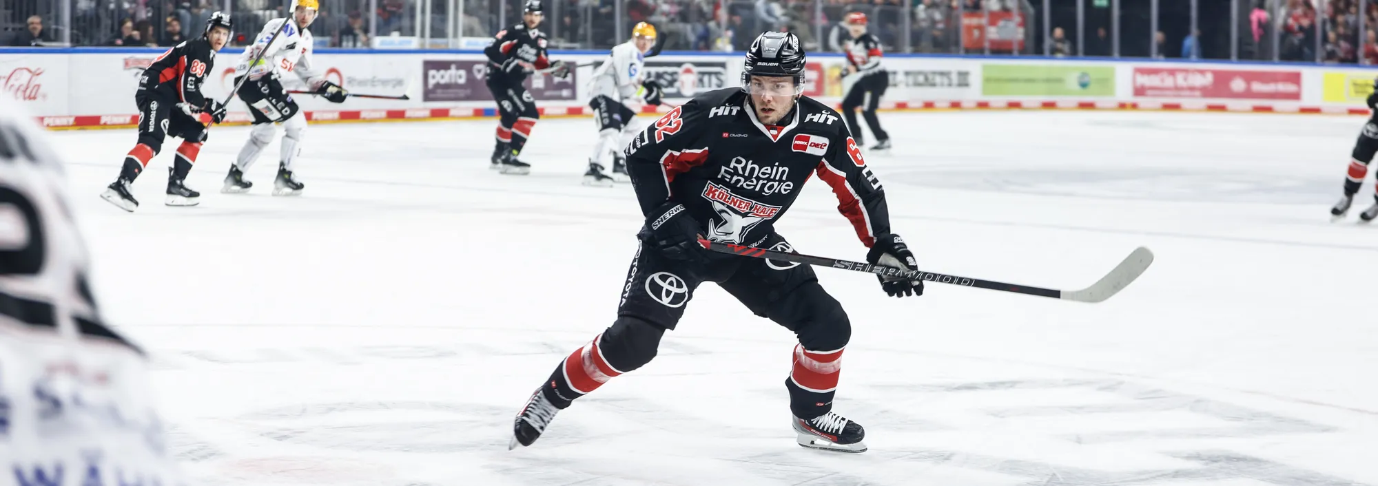 Un giocatore di hockey su ghiaccio in una maglia nera e rossa che scia sul ghiaccio con un bastone da hockey.