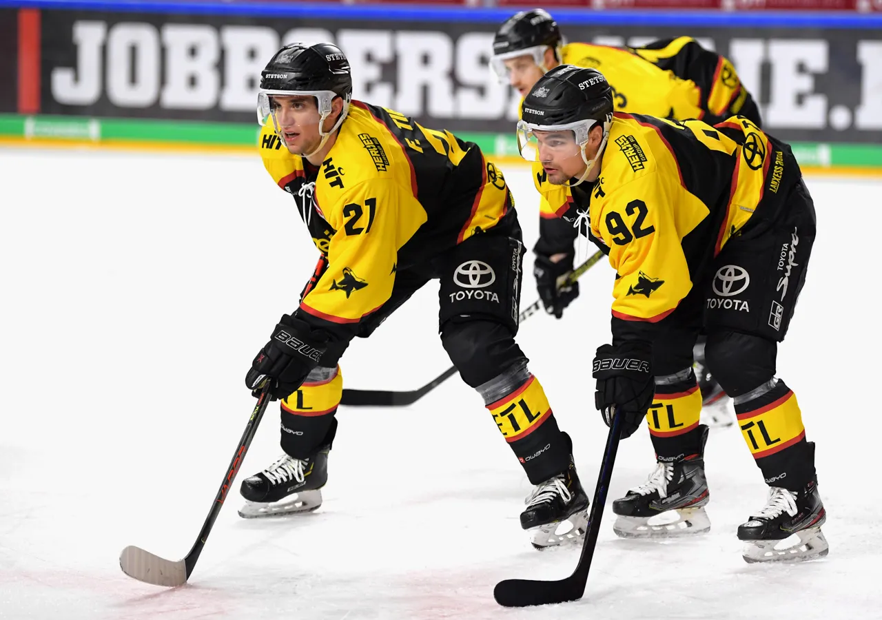 Due giocatori di hockey su ghiaccio con maglie gialle e nere con i numeri 21 e 92 sul ghiaccio, concentrati sulla partita.