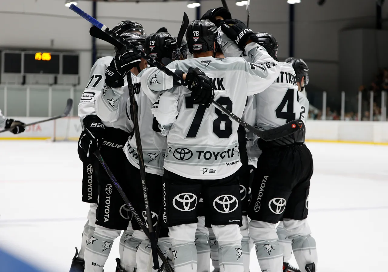 Giocatori di hockey su ghiaccio con maglie bianche con numeri neri e loghi di sponsor, che si abbracciano sul ghiaccio.