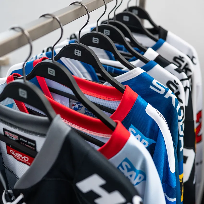 Diverse maglie da hockey su ghiaccio colorate sono appese a un appendiabiti.