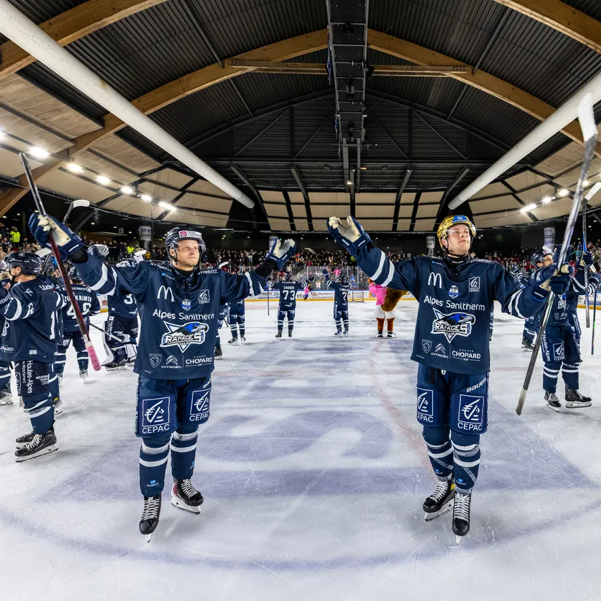 Due giocatori di hockey su ghiaccio sul ghiaccio che celebrano con le loro stecche mentre altri giocatori e spettatori sono visibili sullo sfondo.