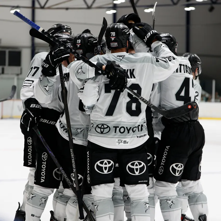 Un gruppo di giocatori di hockey su ghiaccio in magliette bianche e nere si abbracciano sul ghiaccio.