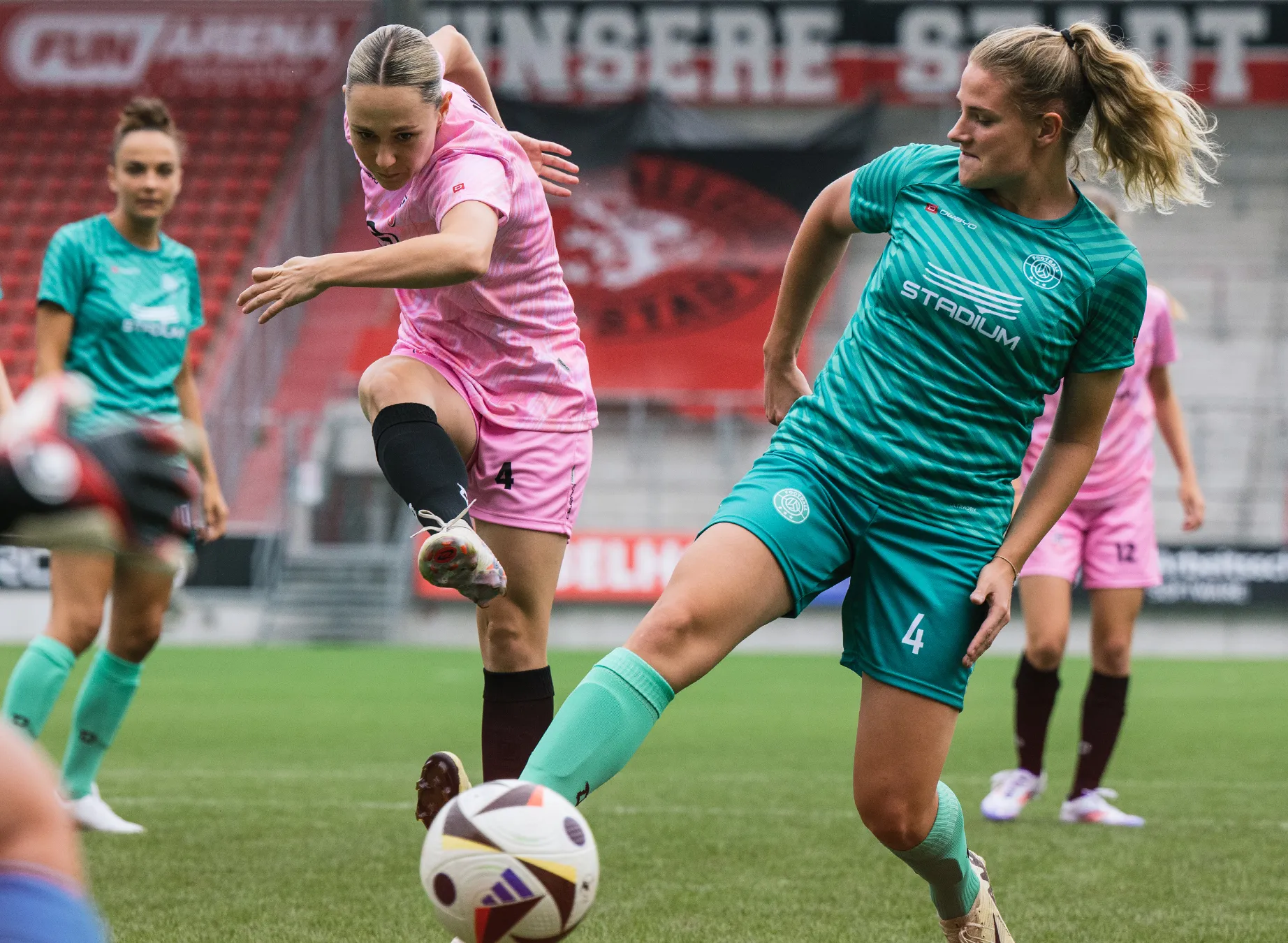 Due donne in maglie sportive colorate stanno giocando a calcio su un campo erboso.