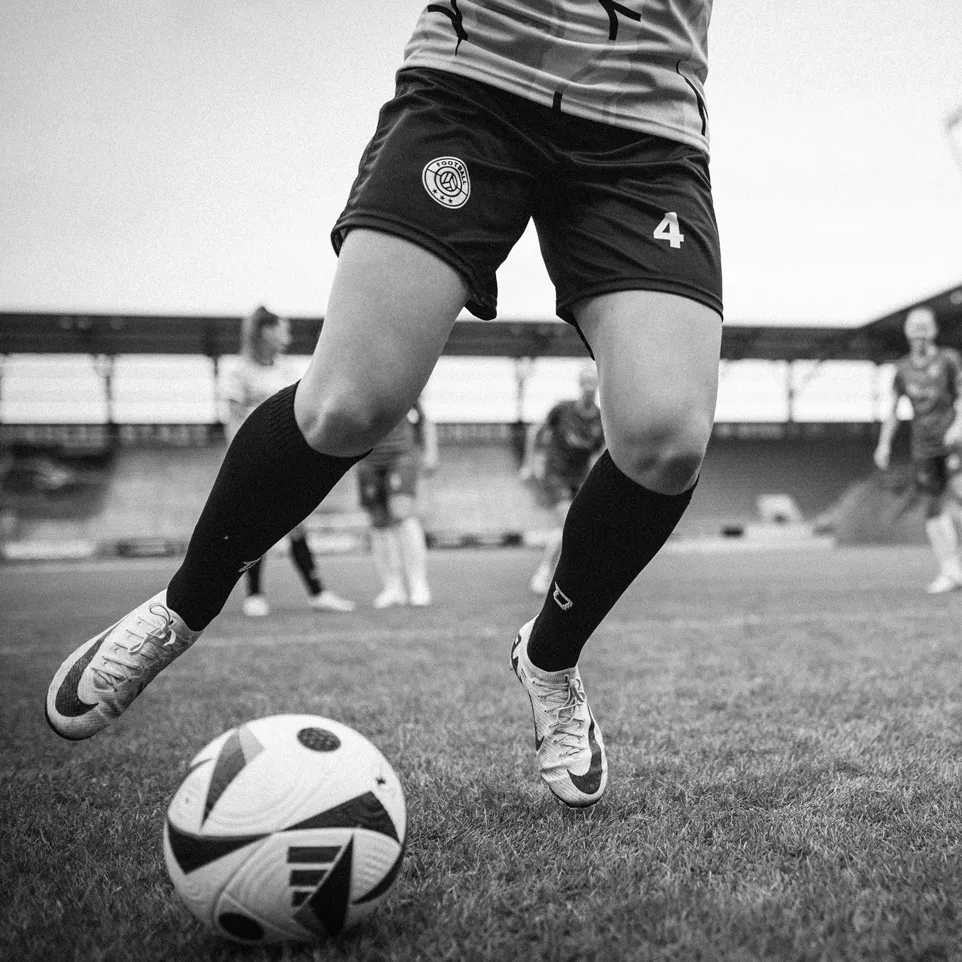 Una giocatrice in pantaloni corti e calzettoni che dribbla un pallone da calcio su un campo d'erba.