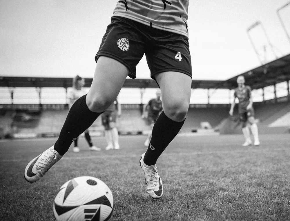 Una calciatrice in pantaloni corti e calze lunghe che gioca con un pallone sul campo.
