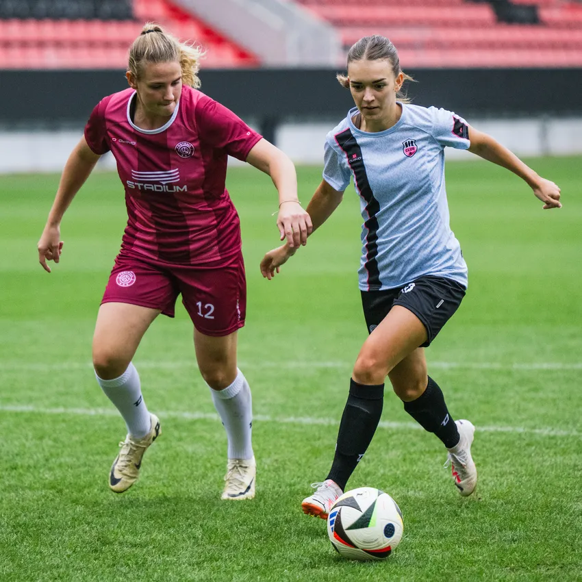 Due donne in abbigliamento sportivo stanno giocando a calcio su un campo verde.