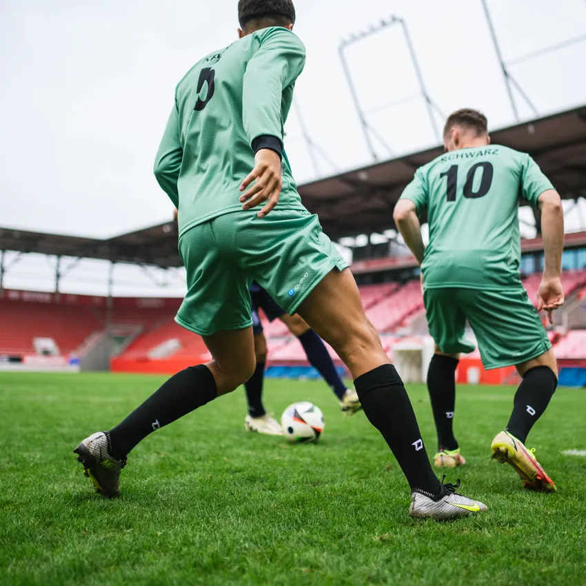 Due calciatori in maglie verdi e calze nere che giocano su un campo d'erba con un pallone.