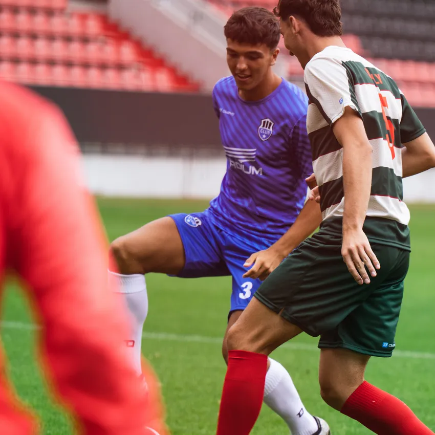 Due calciatori in azione sul campo, uno indossa una maglia blu e l'altro una maglia a righe verdi e rosse.