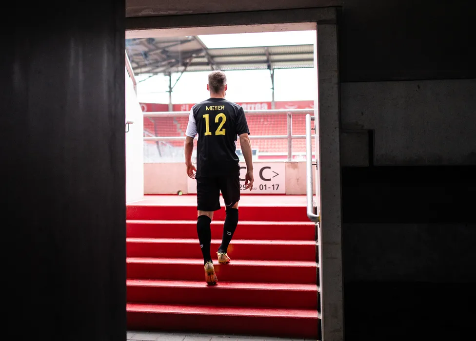 Un calciatore con una maglietta nera con il numero 12 sale le scale rosse dello stadio.