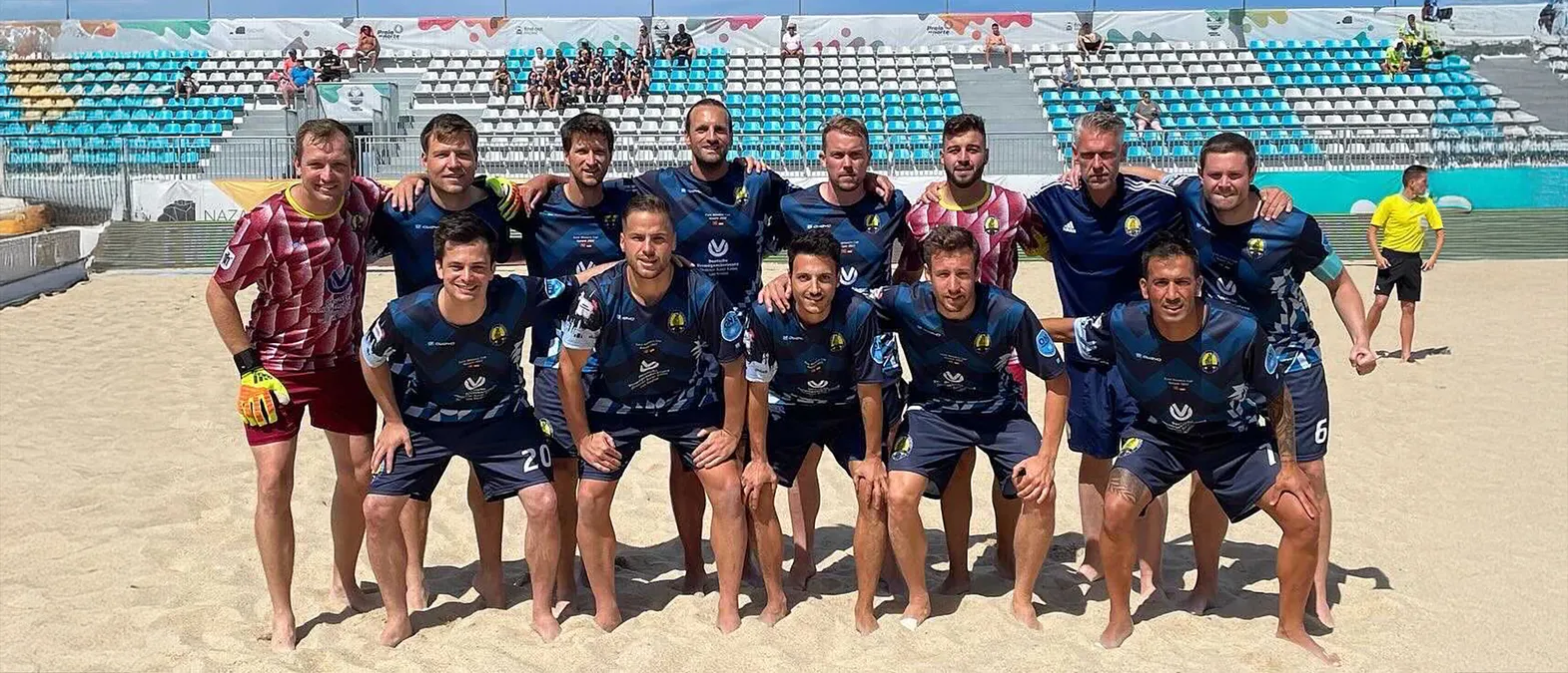 Una squadra di calcio posa su un campo di sabbia con abbigliamento sportivo personalizzato realizzato da owayo.