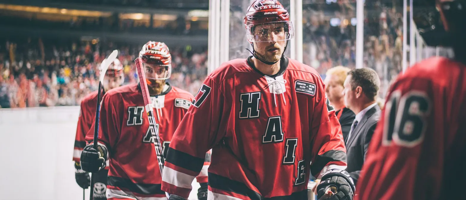 Giocatori di hockey su ghiaccio con maglie rosse con le lettere 'H', 'A', 'I', 'E' e il numero 7 sul retro, in piedi sul ghiaccio.