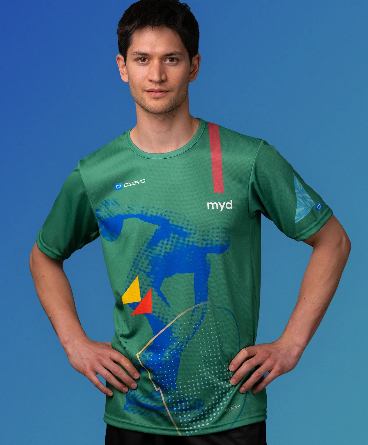 Un uomo indossa una maglia sportiva verde personalizzata di owayo con un design grafico blu, giallo e rosso e la scritta 'myd' sul petto.