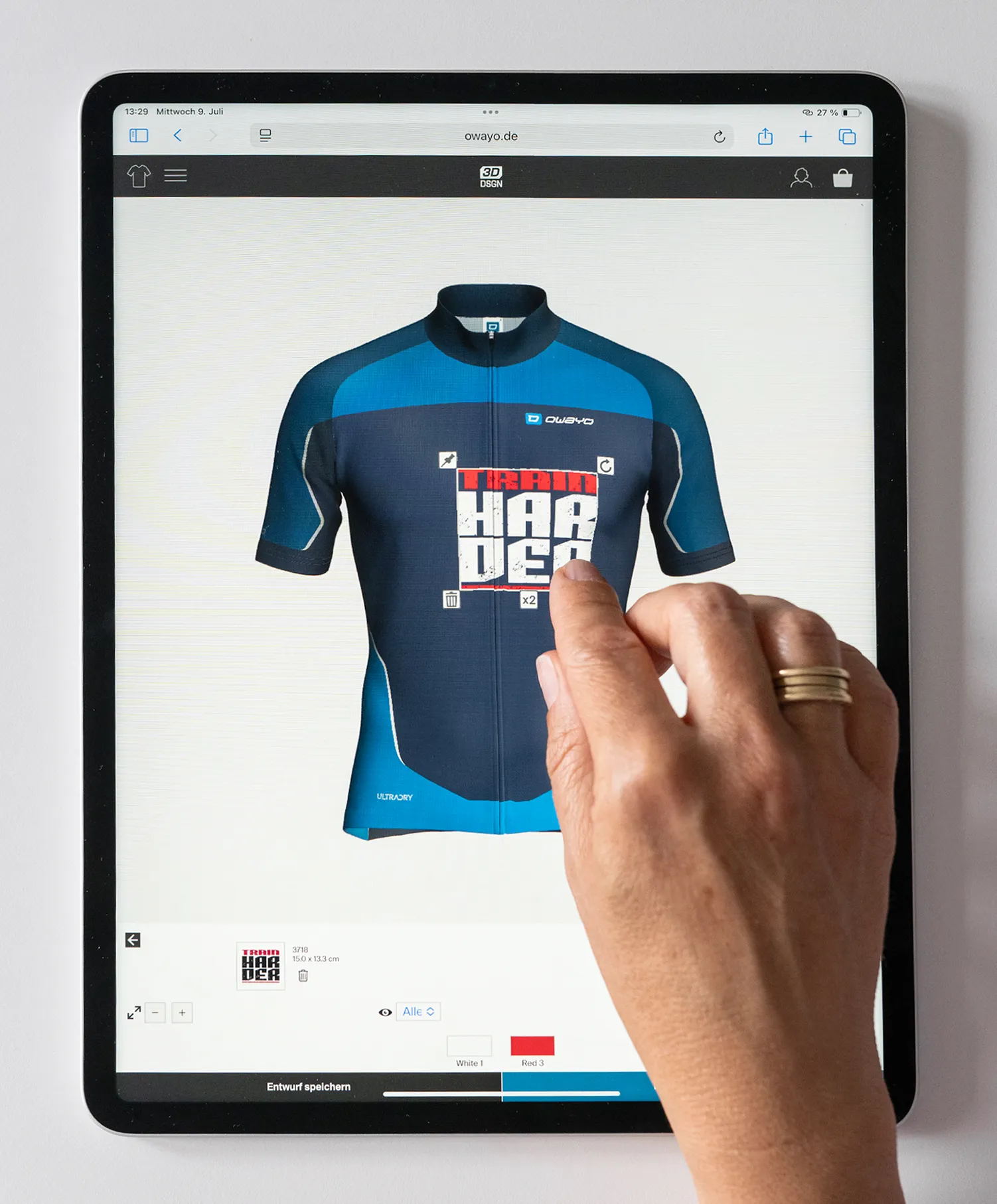 Una mano interagisce con un tablet che mostra il sito web di owayo, visualizzando una maglia da ciclismo personalizzata blu e blu scuro con la scritta 'TRAIN HARDER'.