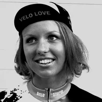 Una donna con capelli biondi corti indossa un berretto da ciclismo nero con la scritta 'VELO LOVE' e una maglia da ciclismo su misura con il nome 'Anja Sturm'.
