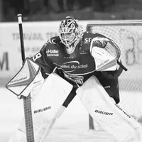 Un portiere di hockey su ghiaccio con attrezzatura completa, inclusi casco, maschera, guanti e gambali, è in posizione difensiva sul ghiaccio.