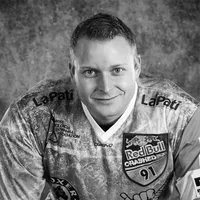 Un uomo indossa una maglia sportiva a motivi con vari loghi di sponsor, tra cui Red Bull e LaPati, e la scritta 'owayo' sul petto.