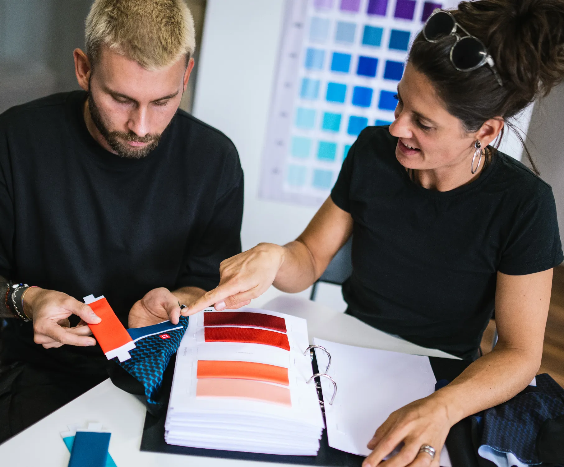 Un uomo e una donna scelgono i colori per abbigliamento sportivo su misura, esaminando campioni di tessuti e tavolozze di colori.