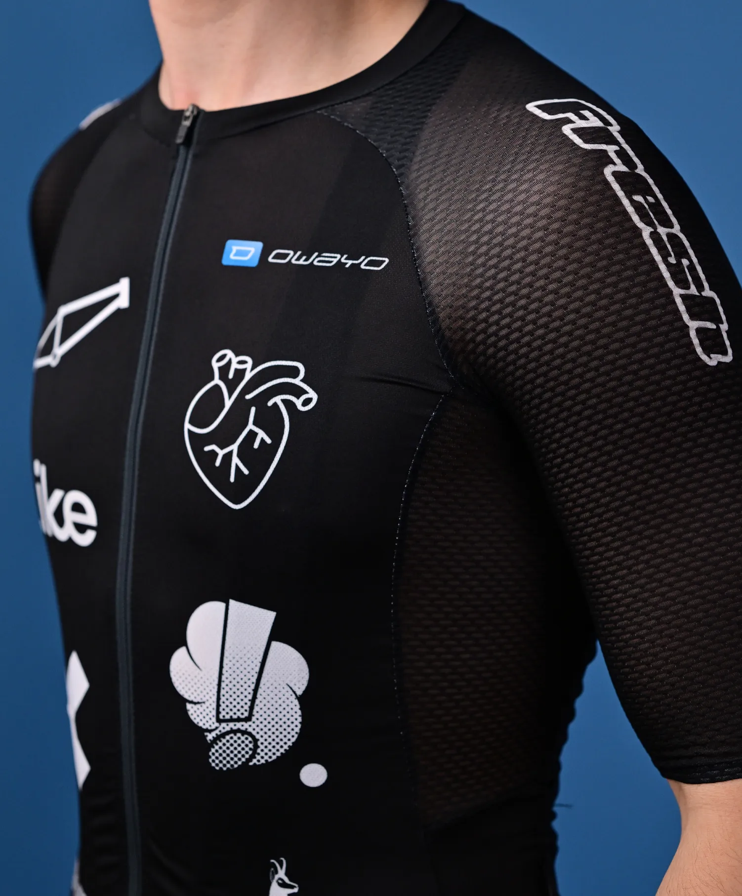 Una persona indossa una maglia sportiva nera senza maniche di owayo con una cerniera frontale, decorata con vari loghi e grafiche bianchi, tra cui un cuore e una 'O' stilizzata, sul petto e sul braccio.