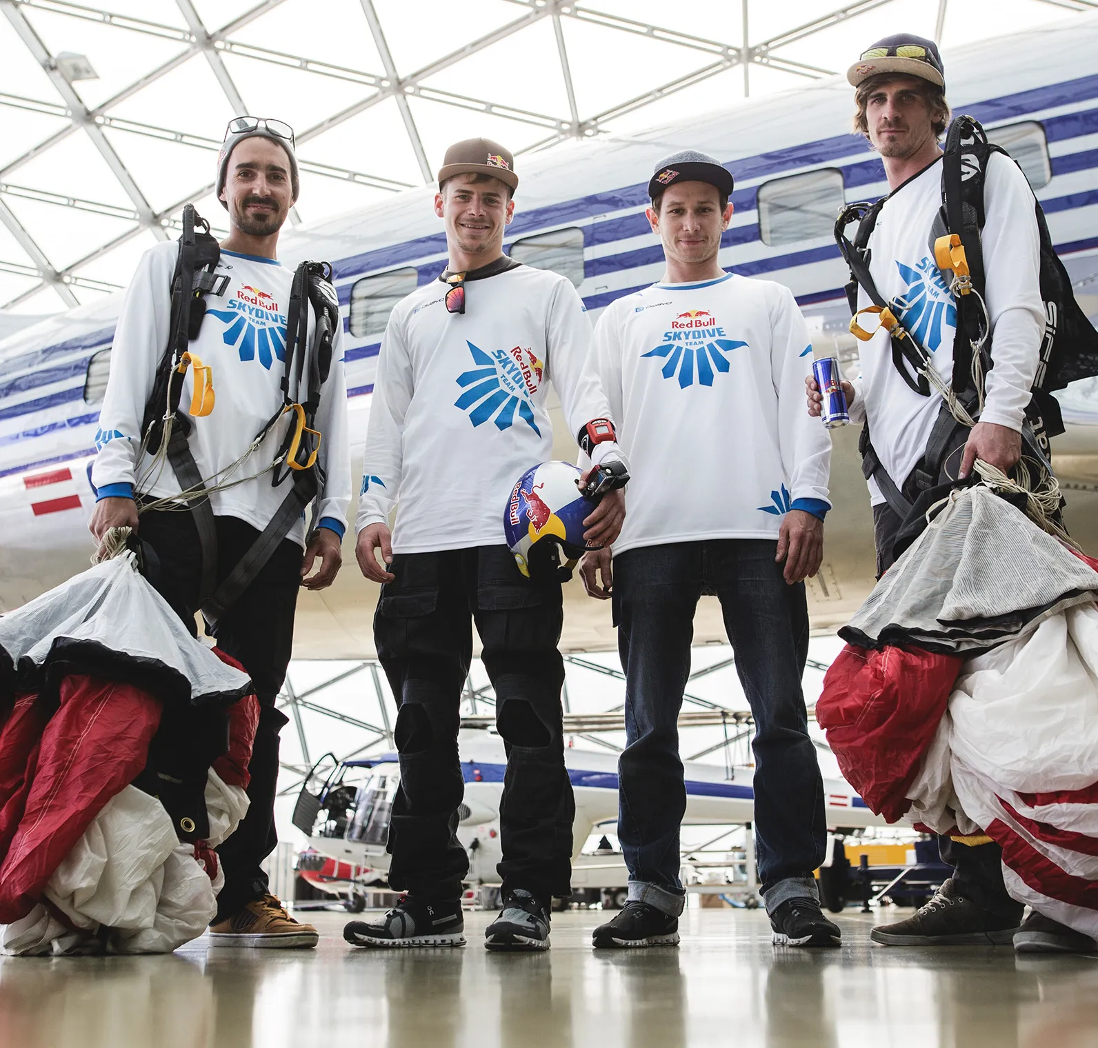 Quattro uomini in magliette bianche a maniche lunghe con il logo della Red Bull Skydive Team stanno in un hangar davanti a un aereo.