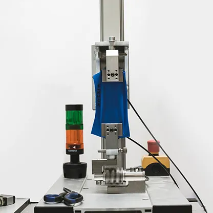 Un tessuto blu viene testato in una macchina su un banco da lavoro, accanto a una luce di segnalazione e attrezzi.