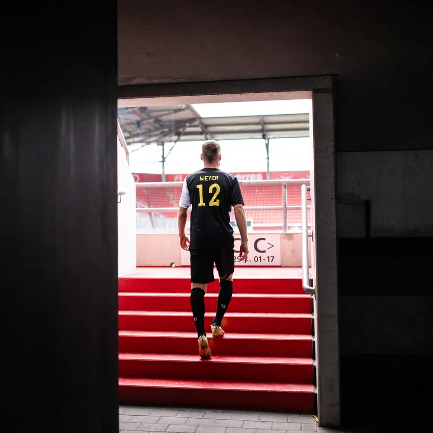Un calciatore in una maglietta nera con il numero 12 sale le scale rosse di uno stadio.