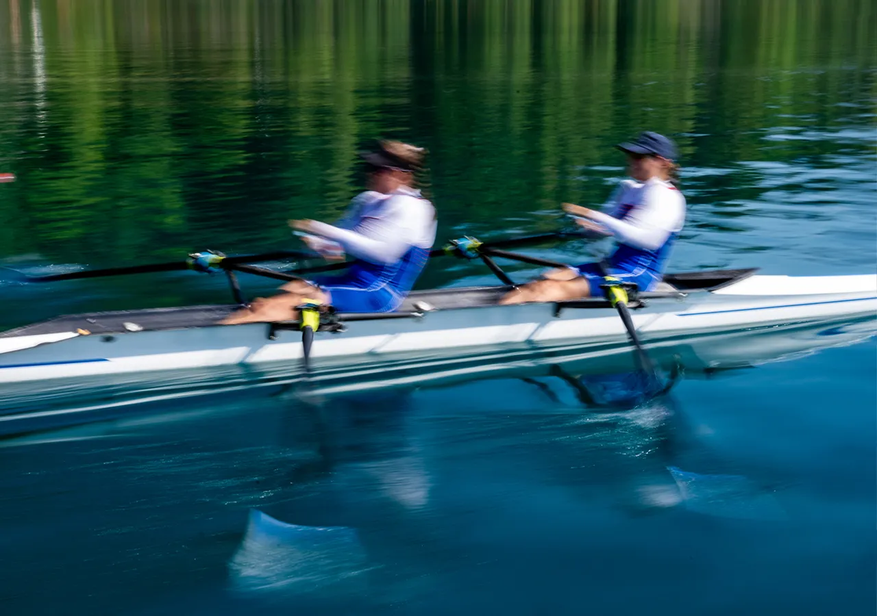 Due rematori in abbigliamento sportivo blu remano in sincronia su una superficie d'acqua calma.