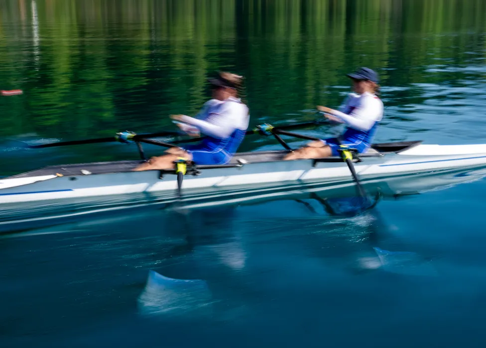 Due rematori in abbigliamento sportivo blu remano all'unisono su acqua calma.