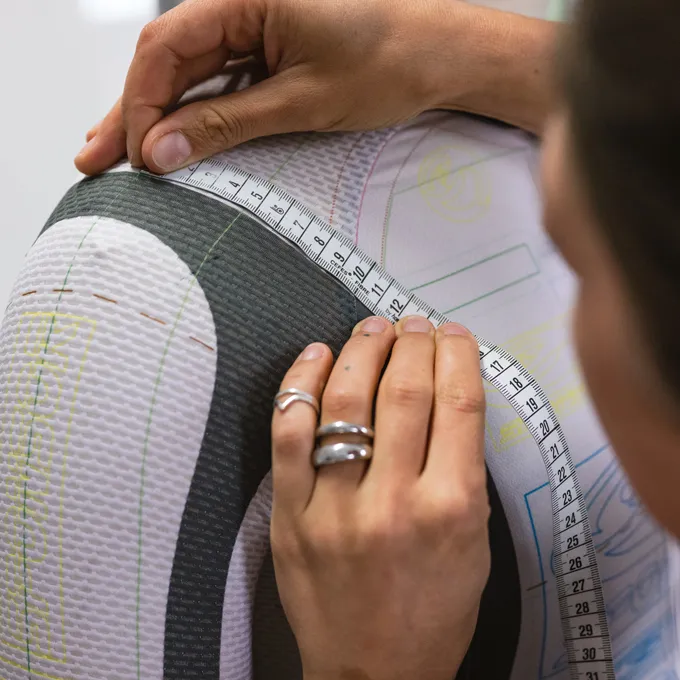 Una persona misura il braccio superiore di un abbigliamento sportivo su misura di owayo, contrassegnato con linee di taglio.