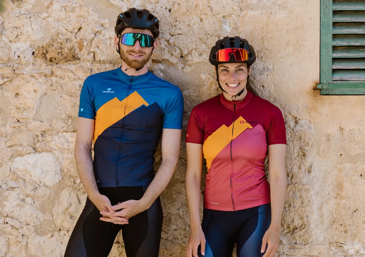 Un uomo e una donna in abbigliamento sportivo personalizzato di owayo, in piedi davanti a un muro di pietra.