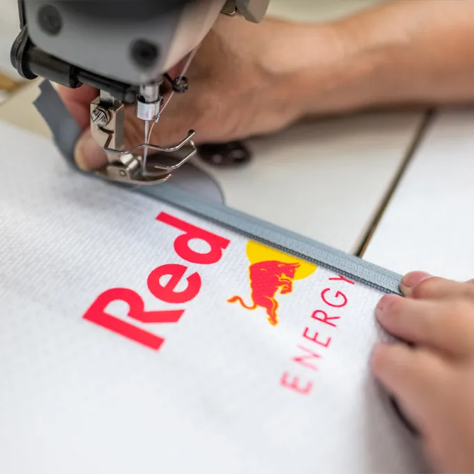 Un primo piano di una macchina da cucire che cuciva un capo sportivo bianco con il logo Red Bull, mentre una persona tiene il tessuto.