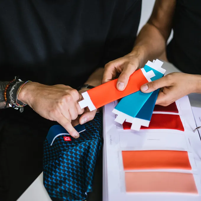 Due persone scelgono campioni di colore per abbigliamento sportivo su misura, con un tessuto blu a motivo e diverse opzioni di colore visibili.